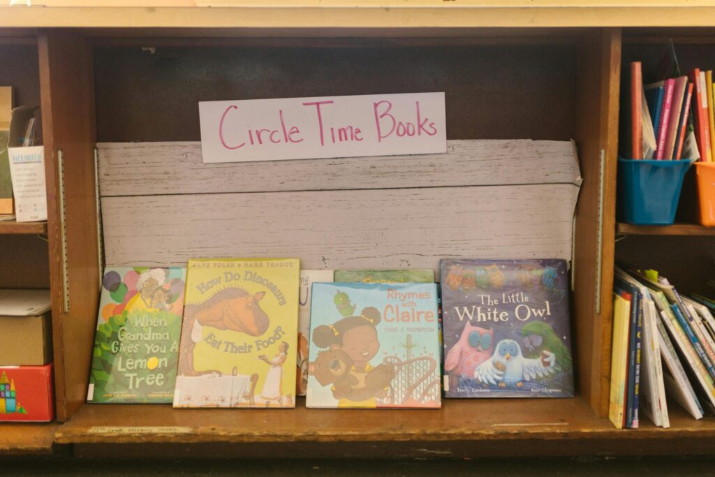 A collection of children's books displayed on a wooden shelf in a library setting.